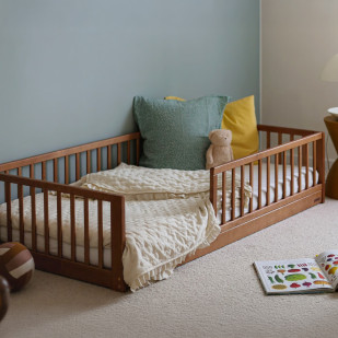Lit au sol Montessori Monty 80x160 en bois finition vintage, avec barrières de sécurité, coussins colorés et peluche dans une chambre douce et cosy.