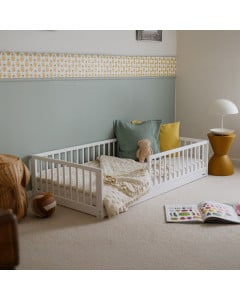 Lit enfant Montessori blanc en bois, modèle Monty 80x160 cm de Woodies, avec barrières de sécurité, coussins colorés, peluche et couverture, dans une chambre décorée de façon douce et moderne.