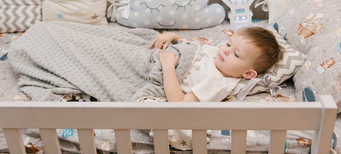 Un jeune enfant dans son lit bébé, entouré de ses peluches et jouets préférés