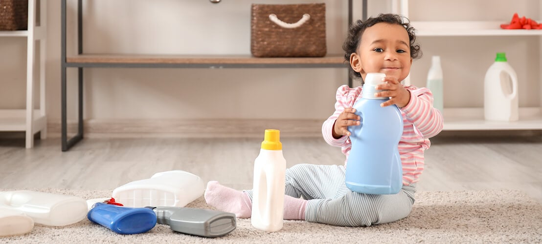Image d'un bébé qui joue avec les emballages des produits de nettoyage que ses parents ont employés pour l'entretien de sa chambre