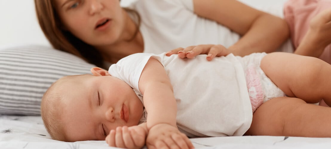 Photo d'une mère qui pratique le cododo regardant sa petite fille endormie
