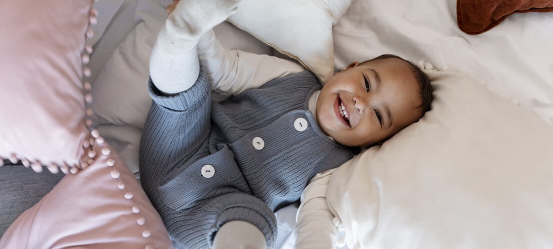 Photo d’un adorable bébé riant et allongé sur le lit entouré d'oreillers