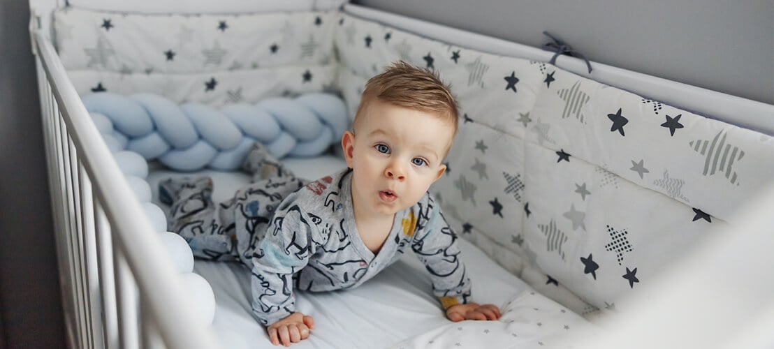 Photo adorable bambin blond aux beaux yeux bleus allongé sur le ventre dans son berceau