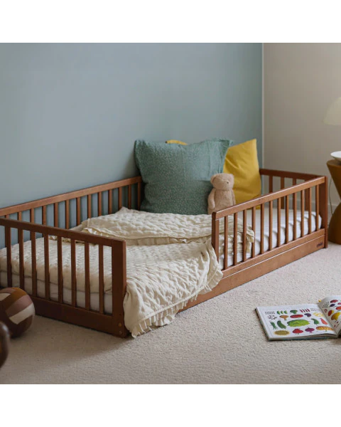 Lit au sol Montessori Monty 80x160 en bois finition vintage, avec barrières de sécurité, coussins colorés et peluche dans une chambre douce et cosy.
